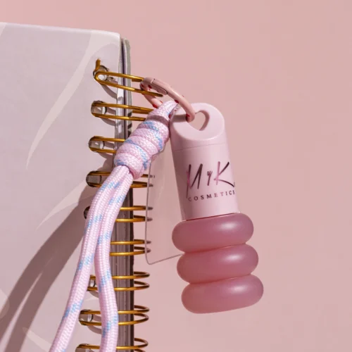 Brillo labial Cute Gloss de MYK Cosmetics colgando como charm de una agenda con cordón rosa.